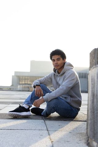 Teen sitting on urban rooftop wearing gray hoodie and jeans checking smartwatch