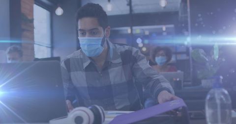 Young man wearing mask working on laptop in modern office