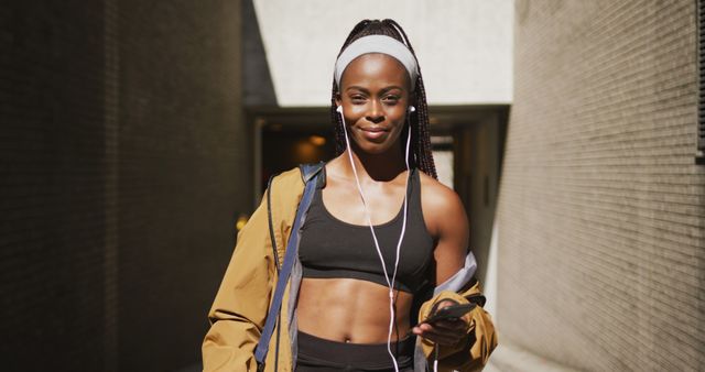 Woman with headphones and smartphone in urban attire during a daytime workout. Ideal for fitness, health, and lifestyle promotions.