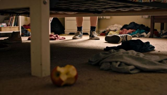 Teen standing under bed wearing high-top sneakers, bitten apple on messy carpet
