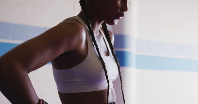 Athletic woman with braids wearing a sport bra stands in gym, looking determined and focused. Ideal for fitness-related ads, health and wellness articles, workout gear promotions, or sports-related content showcasing strength, health, and dedication.