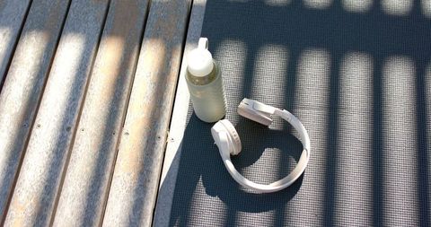 Sunlit headphones and water bottle on yoga mat with weathered wooden deck shadow bands