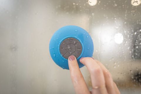 Close-up hand pressing blue waterproof bluetooth shower speaker suctioned to glass