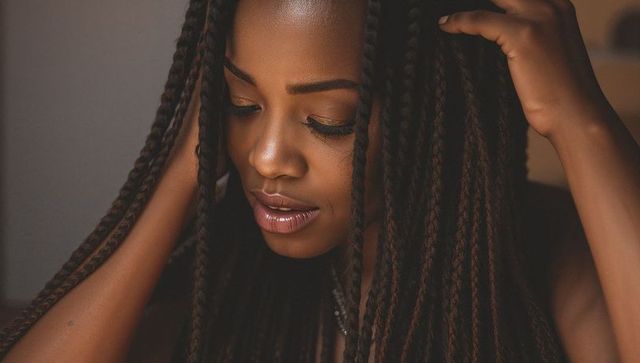 Contemplative african american woman touching box braids, glossy lips, golden eye makeup