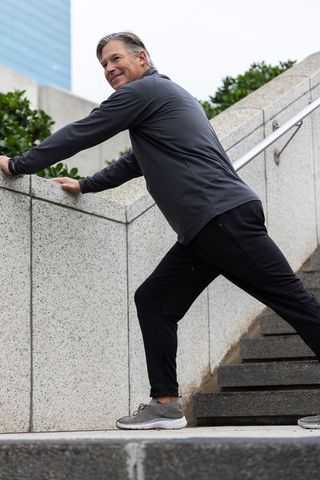 Middle-aged man stretching in urban stairs lunge wearing activewear for outdoor fitness