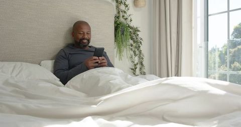 Man enjoying smartphone in cozy bedroom morning light