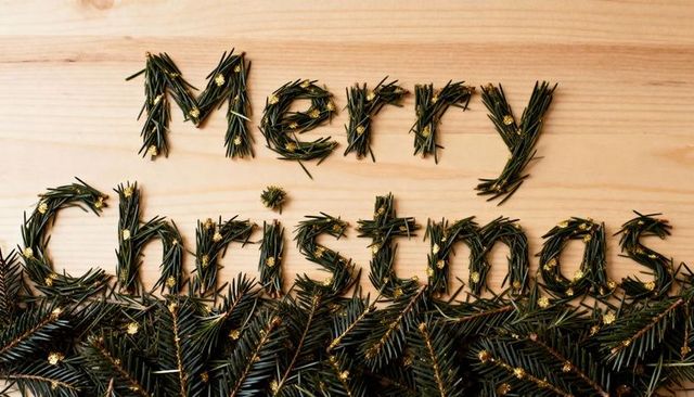 Merry christmas spelled with pine needle letters and gold glitter on light wood background