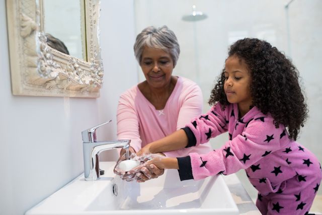 Grandmother and granddaughter washing hands with soap in bathroom sink at home