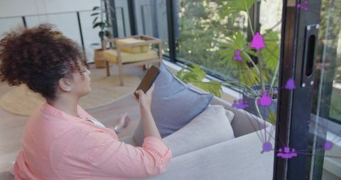 Woman using smartphone on sofa with purple social overlay and sunlit modern balcony
