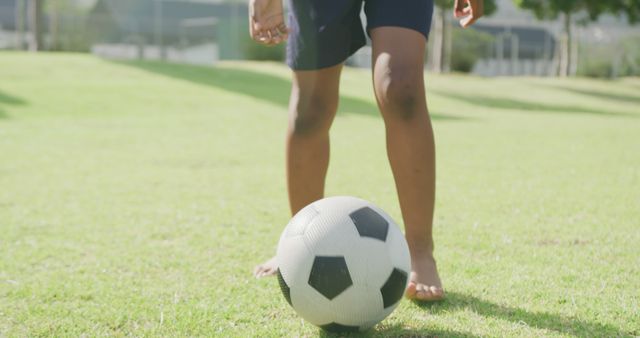 This image of a child standing on a grass field, ready to kick a soccer ball, conveys outdoor sports and leisure activities. The warm weather emphasizes the fun and freedom of summertime play. Ideal for use in promotional materials for children's sports camps, recreational programs, or advertisements highlighting active lifestyles.