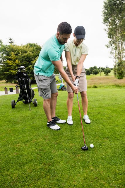 Male instructor assisting woman in learning golf at golf course. Ideal for use in articles or advertisements related to golf training, sports coaching, outdoor activities, teamwork, and leisure activities. Suitable for promoting golf courses, sports equipment, and instructional programs.