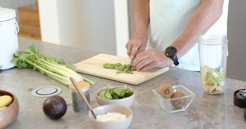 Mature man chopping fresh herbs on kitchen counter preparing healthy smoothie ingredients