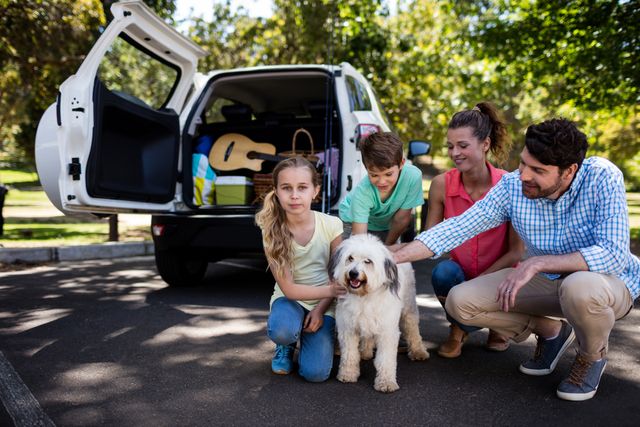 Family with two children and dog preparing for a road trip in a park. Parents and kids bonding with their pet, enjoying outdoor time together. Ideal for themes of family vacations, pet-friendly travel, and outdoor activities.