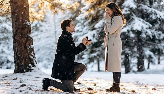 Man proposing in snowy pine forest woman reacting with joy romantic winter engagement