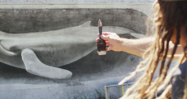 Image of caucasian male artist with dreadlocks measuring proportions of whale mural with paintbrush - Download Free Stock Photos Pikwizard.com