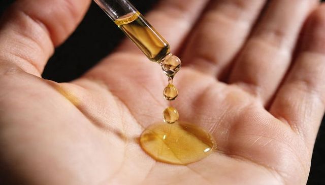 Amber oil droplets falling from glass pipette onto palm macro skincare concept