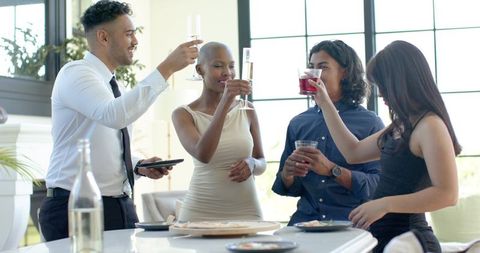 Friends toasting at kitchen island with champagne flutes and flatbread during celebration