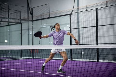 Male padel player jumping for forehand smash on purple indoor court