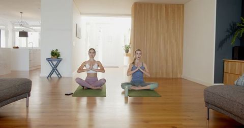 Two women practicing seated meditation in sunlit minimalist living room