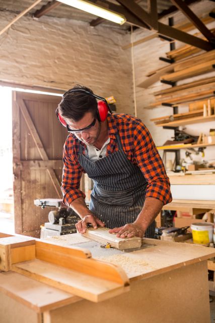 Carpenter focused on his work, wearing safety gear including goggles and ear protection. Ideal for illustrating skilled handiwork, professional craftsmanship, DIY projects, woodworking tutorials, construction industry, or promoting artisan work.