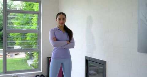 African american woman standing in home gym wearing lavender top and blue leggings