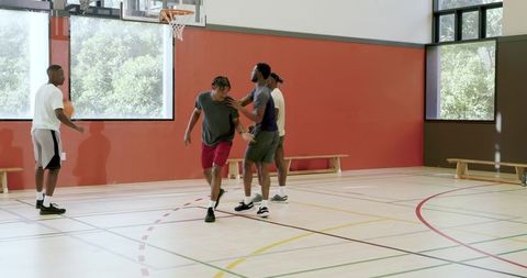Diverse male athletes practicing basketball, dribbling and shooting on indoor gym court