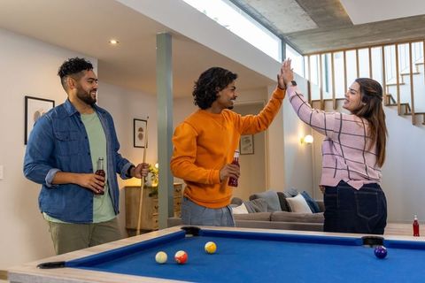 Diverse friends high-fiving while playing pool and enjoying drinks in modern basement