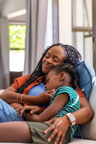 African american mother cuddling daughter on sofa, cozy family bonding moment at home