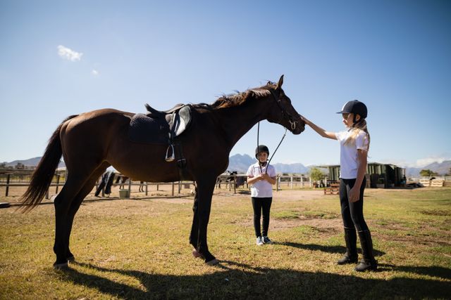 Two girls standing with a horse in the ranch on a sunny day