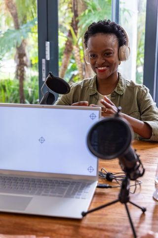 African american woman podcasting with headphones and desktop microphone in home studio