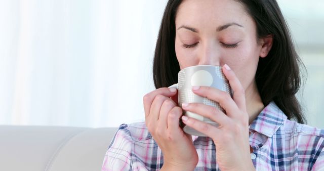 A middle-aged Caucasian woman enjoys a warm beverage from a mug, with copy space. Her closed eyes and serene expression suggest a moment of relaxation or a break from daily activities.