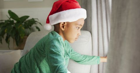Young Boy in Santa Hat Gazing Out Window During Christmas