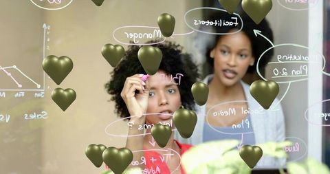 Female Colleagues Collaborating on Glass Board Drawing Flowchart with Gold Heart Overlays