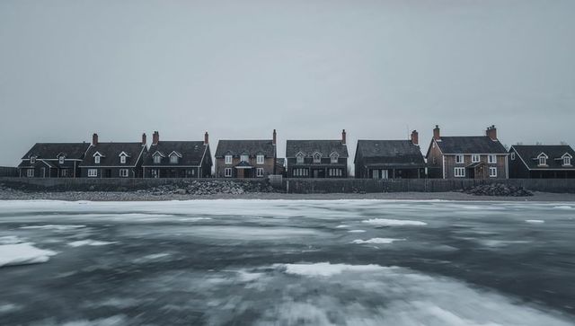 Desaturated seafront cottages lining frozen shoreline, overcast winter, ice and chimneys