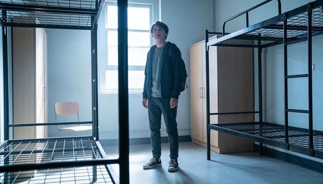 Young student standing in empty dorm room looking up toward window with bunk beds