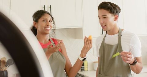 Young couple tasting fresh ingredients in bright modern kitchen wearing aprons