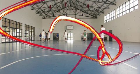 Men playing indoor basketball on blue court with neon light trails conveying motion energy