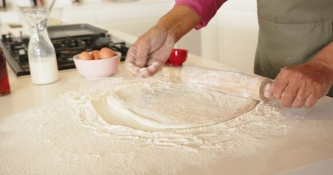 Mature man rolling dough on floured countertop with rolling pin for homemade baking