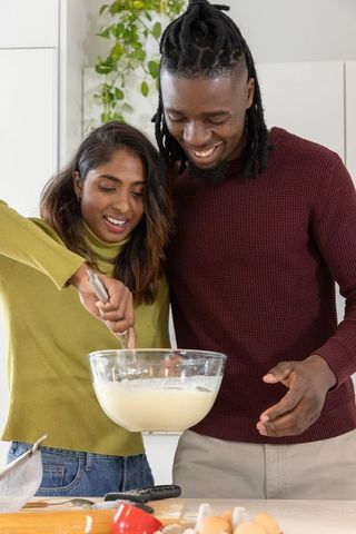 Mixing batter, mixed-ethnicity couple baking together in bright cozy kitchen