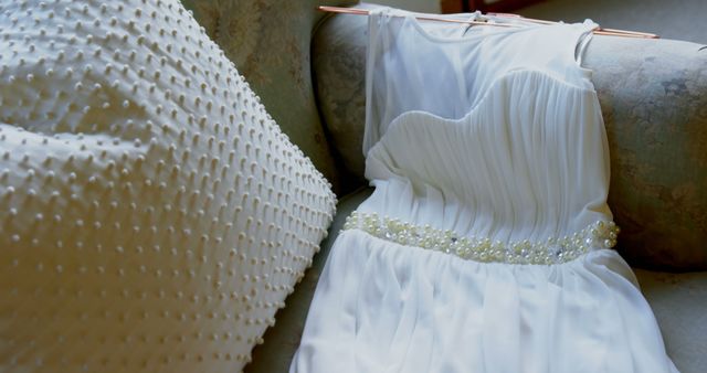 Close up of white wedding dress with pearls lying on couch. Wedding, celebration and jewellery.
