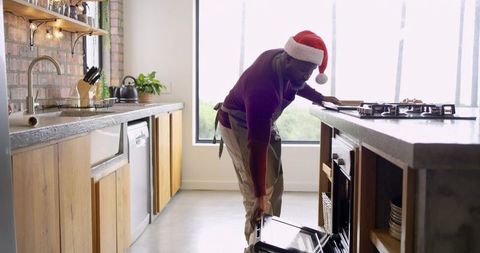 African American Man Wearing Santa Hat Pulling Oven Door in Modern Rustic Kitchen