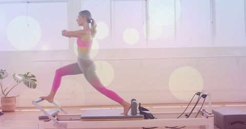 Woman performing lunge on pilates reformer in sunlit studio for strength and balance