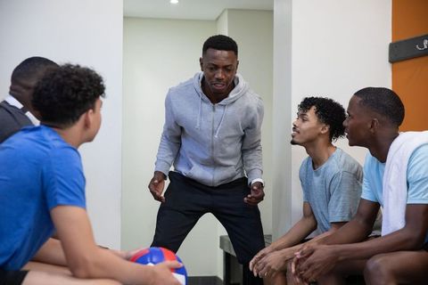 African american coach motivating teen basketball team during locker room huddle