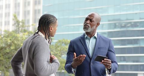 Senior african american executive mentoring young male colleague in urban plaza with tablet