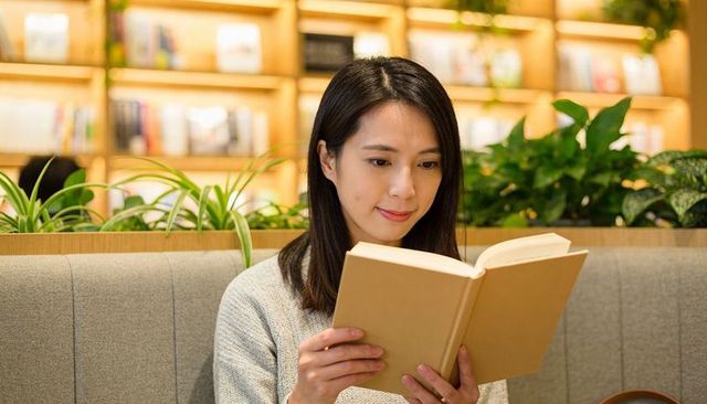 Young woman reading paperback in cozy cafe lounge with warm lighting and bookshelves