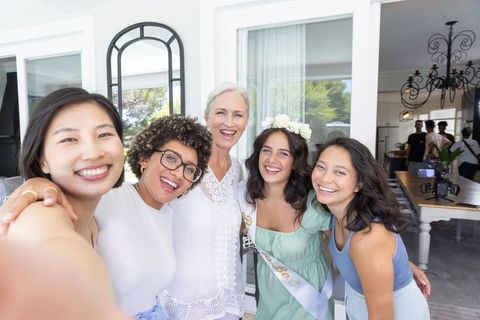 Smiling bride-to-be posing with diverse friends, celebrating bachelorette brunch at home