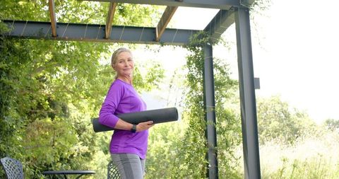Active Senior Woman Holding Yoga Mat in Verdant Garden