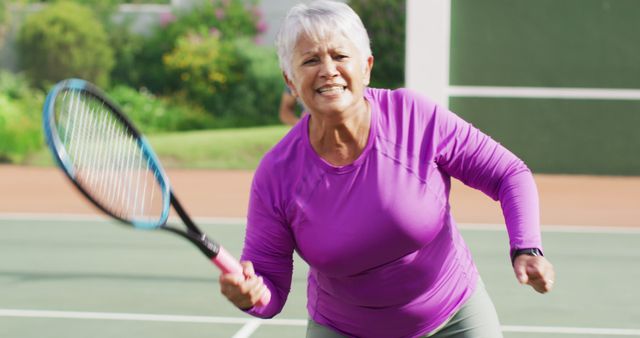 Image of happy biracial senior woman jumping with joy during tennis training. active retirement lifestyle, senior relationship and tennis training concept.