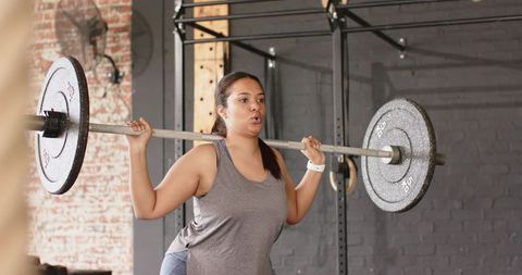 Female athlete performing heavy barbell squat at crossfit rig showcasing strength, focus