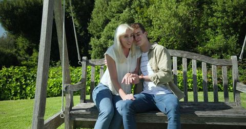 Young Couple Sitting on Wooden Swing in Sunny Garden Having a Happy Moment